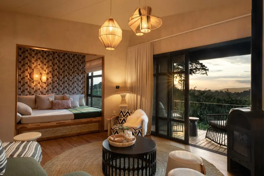Stylish lodge room with a daybed, soft lighting, and a private deck looking out over forested highlands at sunset | Go2Africa